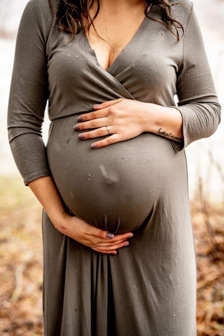 A pregnant woman in a gray dress holding her belly.