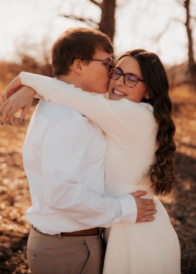 A man and woman hugging in the woods.