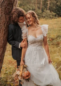 A man and woman in wedding attire standing next to a tree.