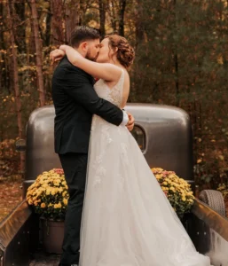 A bride and groom kissing in front of an old car.