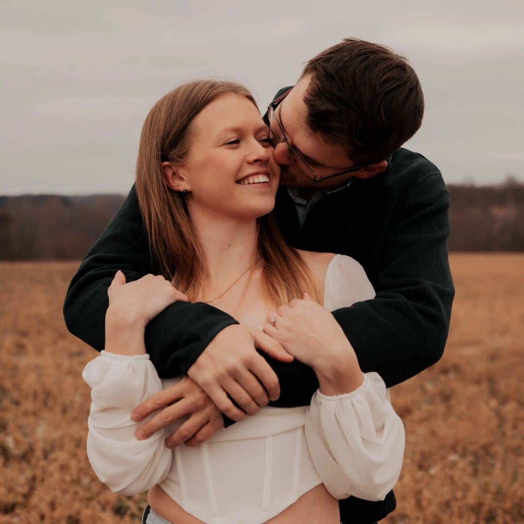 A man and woman kissing in the middle of an open field.