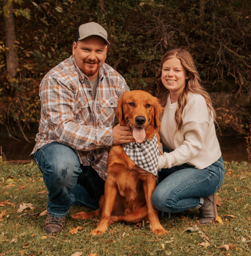 A man and woman sitting on the ground with their dog.