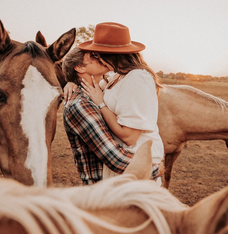 A woman in plaid pants and a cowboy hat standing next to two horses.