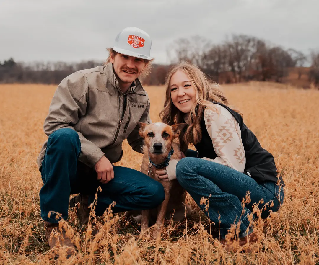 A man and woman sitting in the grass with their dog.