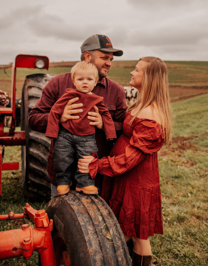 A man and woman holding a child in front of an old tractor.