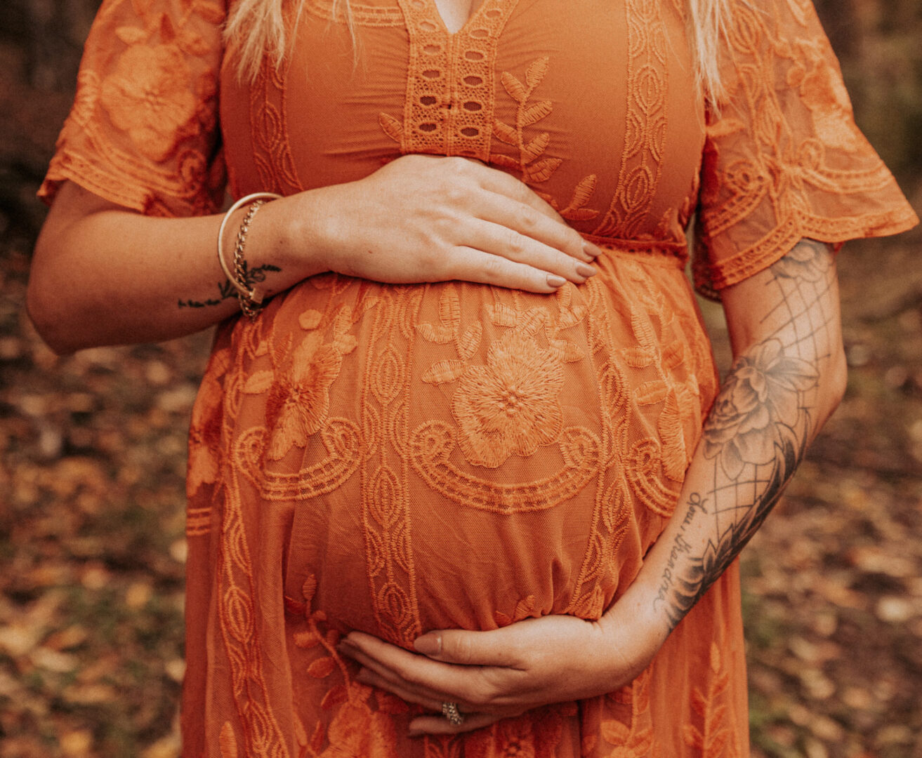 A woman in an orange dress holding her pregnant belly.