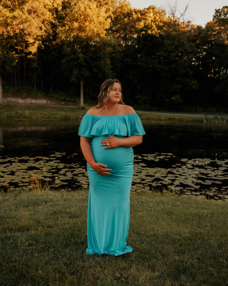 A pregnant woman in a blue dress standing on the grass.