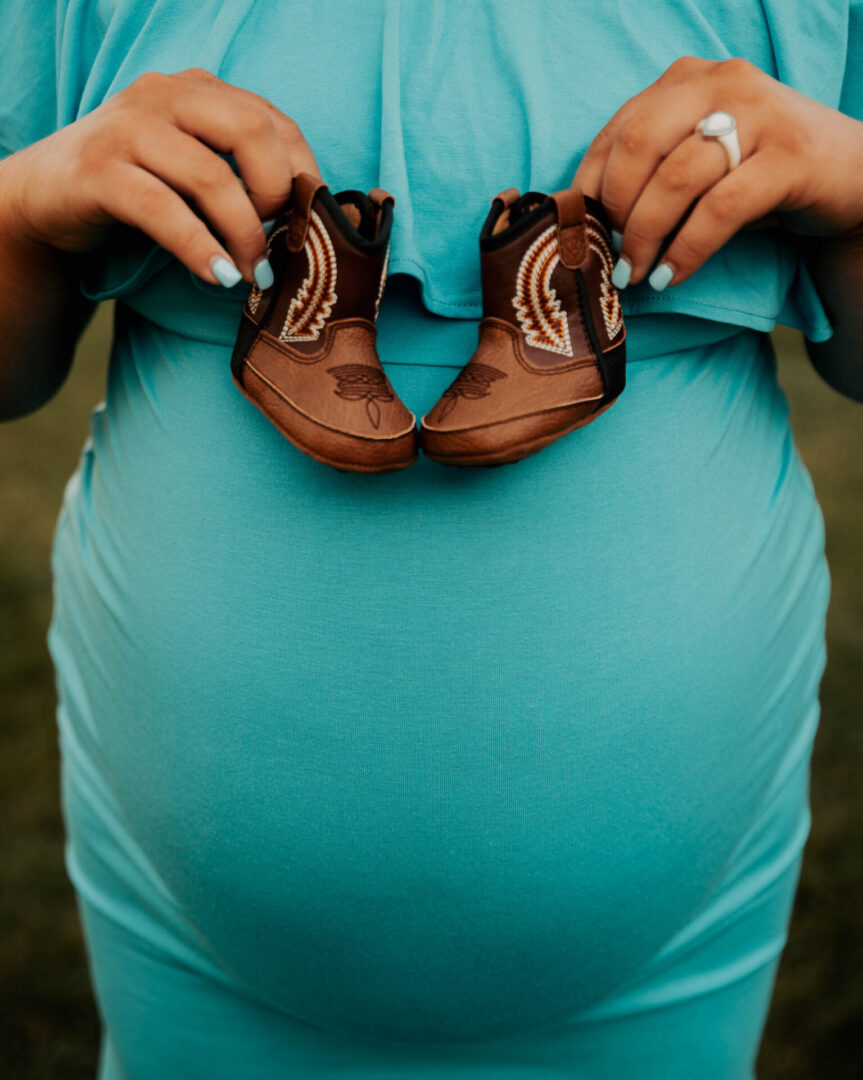 A pregnant woman holding her baby 's shoes.