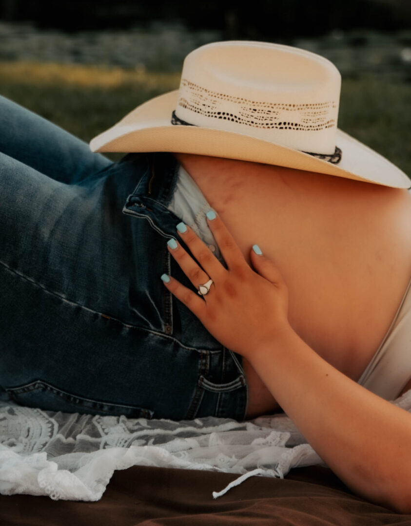 A woman in jeans and a cowboy hat laying on the ground.