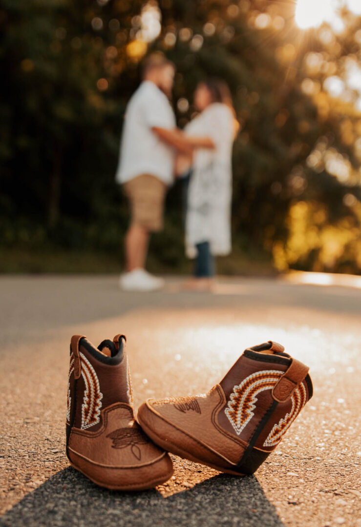 A pair of cowboy boots on the ground with two people in background.