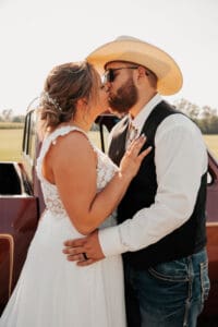 A man and woman kissing in front of an old truck.