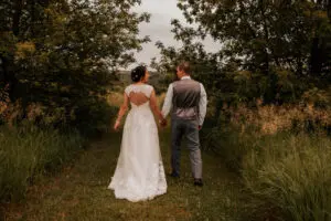 A bride and groom holding hands while walking through the woods.