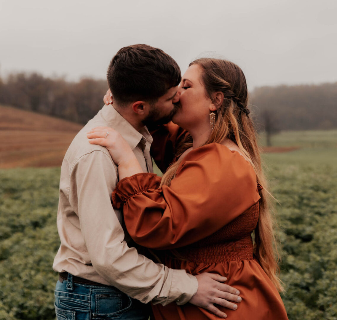 A man and woman kissing in an open field.