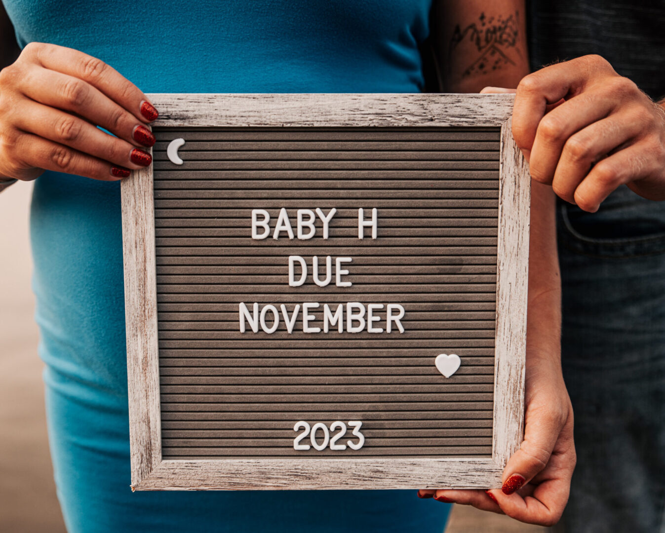 A woman holding a sign that says baby h due november 2 0 2 3.