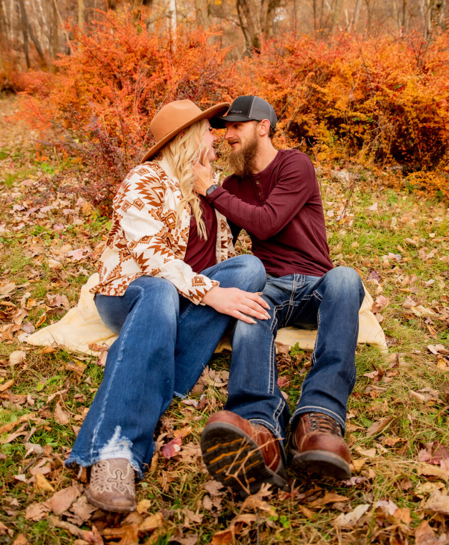 A man and woman sitting on the ground in front of bushes.