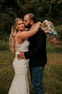 A man and woman kissing in the grass.