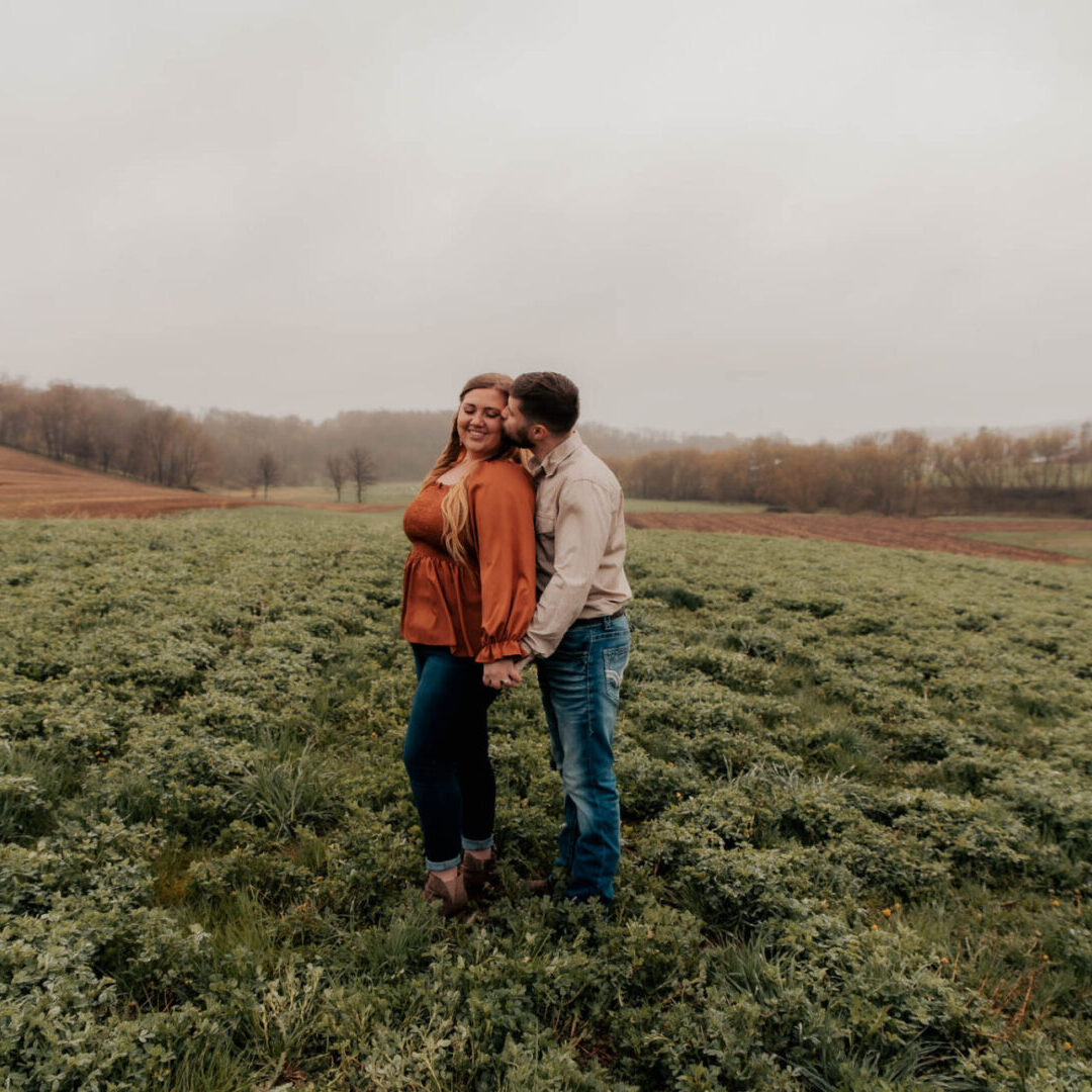 A man and woman kissing in the middle of a field.